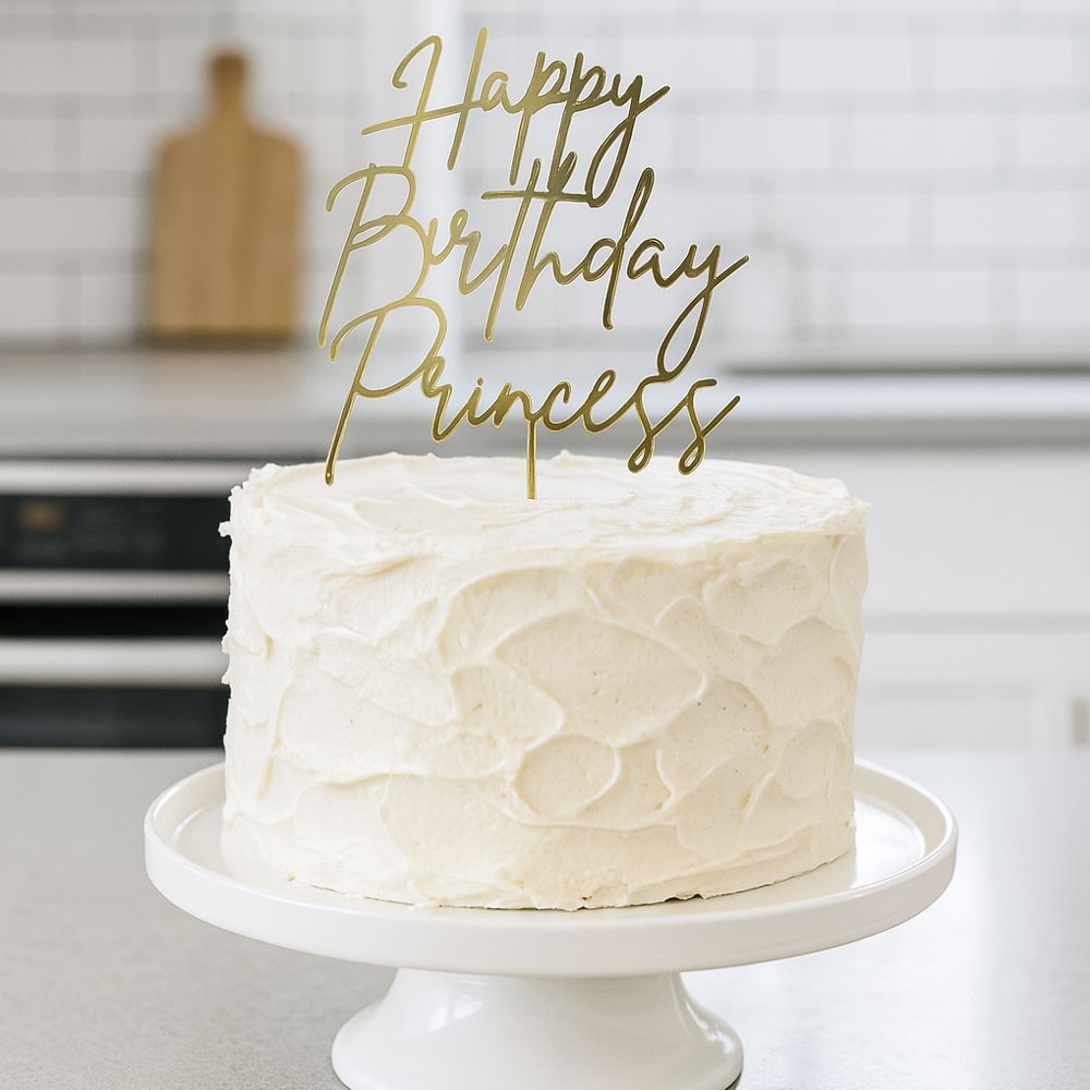Topper Happy Birthday Princess de cartulina espejo dorado decorando una tarta blanca en una cocina luminosa.